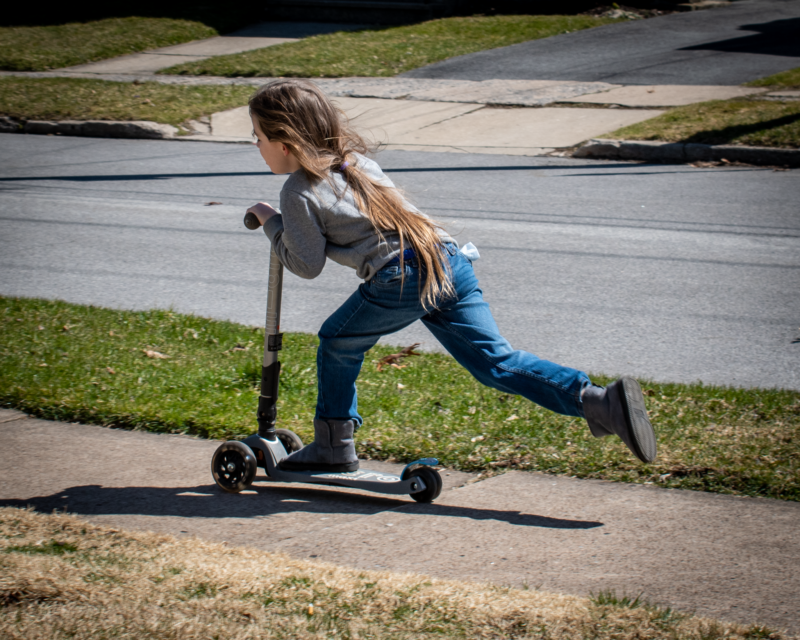 kid on a scooter moving along sidewalk